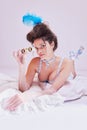 Attractive young woman with opera glasses in vintage lingerie lying on bed against pastel background. Elegant boudoir Royalty Free Stock Photo