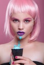 Attractive young woman with pink bob cut and purple lips eating blue ice cream on pink background