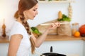 An attractive young woman preparing soup by new keto recipe while standing and smiling in sunny kitchen. Cooking and