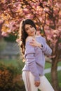 Attractive young woman in a purple sweater stand in front of sakura tree in the park Royalty Free Stock Photo