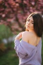 Attractive young woman in a purple sweater stand in front of sakura tree in the park Royalty Free Stock Photo