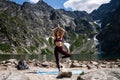 Attractive young woman in red sportswear doing yoga pose for balance and stretching near the lake high in the mountains Royalty Free Stock Photo