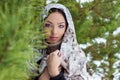 Attractive young woman with a scarf on her head in the winter forest near fir trees, snow falling Royalty Free Stock Photo