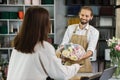 Attractive young woman shopping and buying bouquet in bearded male florist in flower shop. Royalty Free Stock Photo