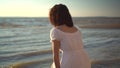 An attractive young woman sits on the beach and looks at the sea. The girl in a white dress sits with her back. Royalty Free Stock Photo