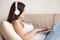Attractive young woman sitting on couch wearing headphones, usin Royalty Free Stock Photo