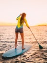 Attractive young woman stand up paddle surfing with beautiful sunset or sunrise colors Royalty Free Stock Photo