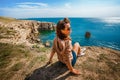 Attractive young woman stands on a high cliff overlooking the rocky cliffs arches on the beach and turquoise sea water on the coas Royalty Free Stock Photo