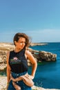 Attractive young woman stands on a high cliff overlooking the rocky cliffs arches on the beach and turquoise sea water on the coas Royalty Free Stock Photo