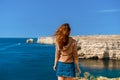 Attractive young woman stands on a high cliff overlooking the rocky cliffs arches on the beach and turquoise sea water on the coas Royalty Free Stock Photo