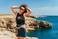Attractive young woman stands on a high cliff overlooking the rocky cliffs arches on the beach and turquoise sea water on the coas Royalty Free Stock Photo