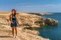 Attractive young woman stands on a high cliff overlooking the rocky cliffs arches on the beach and turquoise sea water on the coas Royalty Free Stock Photo