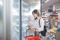 Attractive young woman stands at the refrigerator in the store with frozen food in his hands