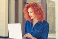 Attractive young woman student in profile, working on laptop, browsing, sitting outdoors. Thoughtful daydreaming girl with red Royalty Free Stock Photo