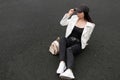Attractive young woman in stylish ripped jeans in a leather jacket in a t-shirt with a gold backpack in fashionable sneakers Royalty Free Stock Photo