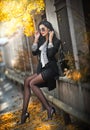 Attractive young woman with sunglasses in autumnal fashion shot. Beautiful lady in black and white outfit with short skirt sitting Royalty Free Stock Photo
