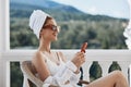 Attractive young woman in sunglasses sits on the balcony and uses the phone Lazy morning Royalty Free Stock Photo