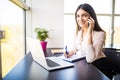 Attractive young woman talking on the mobile phone and smiling while sitting at her working place in office and looking at camera Royalty Free Stock Photo