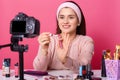 Attractive young woman tests some beauty products and shows lip gloss in her blog. Beauty vlogger sits in front of camera and hods