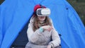 Attractive young woman tourist in a red hat sits in a tourist tent and enjoys a virtual reality helmet