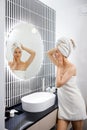 Attractive young woman in towel is looking at mirror standing in bathroom after taking shower. Beauty and Skincare concept Royalty Free Stock Photo