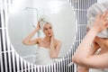 Attractive young woman in towel is looking at mirror standing in bathroom after taking shower. Beauty and Skincare concept Royalty Free Stock Photo