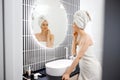 Attractive young woman in towel is looking at mirror standing in bathroom after taking shower. Beauty and Skincare concept Royalty Free Stock Photo