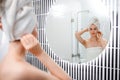 Attractive young woman in towel is looking at mirror standing in bathroom after taking shower. Beauty and Skincare concept Royalty Free Stock Photo