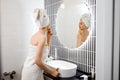 Attractive young woman in towel is looking at mirror standing in bathroom after taking shower. Beauty and Skincare concept Royalty Free Stock Photo