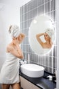 Attractive young woman in towel is looking at mirror standing in bathroom after taking shower. Beauty and Skincare concept Royalty Free Stock Photo