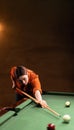 Attractive young woman trying to hit the ball in billiard. Billiard room on the background. Royalty Free Stock Photo