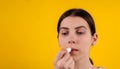 Attractive young woman using hygienic lipstick on yellow background. lips care and protection. woman applying balm on lips Royalty Free Stock Photo