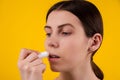 Attractive young woman using hygienic lipstick on yellow background. lips care and protection. woman applying balm on lips