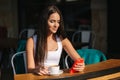 Attractive young woman using phone in cafe on terrace. Social distancing. Beautiful brunette girl chatting and drink Royalty Free Stock Photo