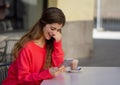 Attractive young woman using smart mobile phone dating app in a coffee shop outside terrace