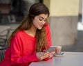 Attractive young woman using smart mobile phone dating app in a coffee shop outside terrace