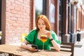 Attractive young woman using typing cellphone, drinking cocktail through straw sitting at table in outdoor cafe terrace Royalty Free Stock Photo