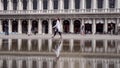 Attractive young woman walk on the square of Sanmarco whit water reflection in Venice Italy