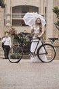 Attractive young woman walking along road with vintage bicycle and red roses