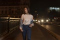 Attractive young woman walking on night street. Stylish girl in white t-shirt, evening city street background Royalty Free Stock Photo