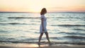 Attractive young woman walks along the sea beach at sunset. A girl in a white dress walks barefoot along the beach. Royalty Free Stock Photo