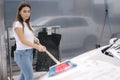 Attractive young woman washing her car with shampoo and brushes. Female washes automobile with foam and water outside on Royalty Free Stock Photo