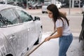 Attractive young woman washing her car with shampoo and brushes. Female washes automobile with foam and water outside on Royalty Free Stock Photo