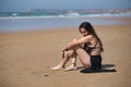 Attractive young woman, wearing black swimsuit and sarong, lonely, quiet and sad, sitting on the shore of the beach. Concept Royalty Free Stock Photo