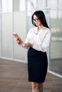 Attractive young woman wearing glasses and reading her touchscreen tablet while standing inside commercial building Royalty Free Stock Photo