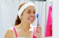 Attractive young woman wearing pink top and white headband, applying brush to face, looking in mirror smiling Royalty Free Stock Photo