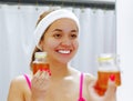 Attractive young woman wearing pink top and white headband, holding up jar of honey, looking in mirror smiling Royalty Free Stock Photo