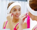 Attractive young woman wearing pink top and white headband, picking eyebrows with tweezers, looking in mirror smiling Royalty Free Stock Photo