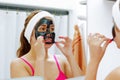 Attractive young woman wearing pink top and white headband, removing black mask treatment from face using hands, looking Royalty Free Stock Photo