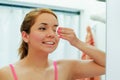 Attractive young woman wearing pink top and white headband, using cotton patch to clean around eye, looking in mirror Royalty Free Stock Photo